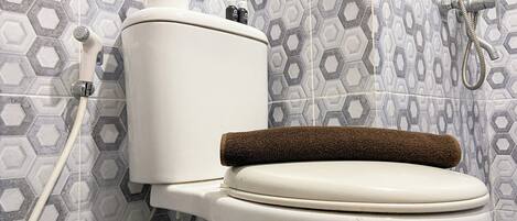 A toilet with a brown bath mat, a shower hose, and a toilet paper holder.