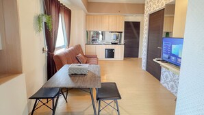 A modern living room with a sofa, a dining table with two chairs, a kitchen area with cabinets and appliances, and a TV on a stand. - Simply And Good Place 2Br At Tamansari Prospero Apartment (Sidoarjo)