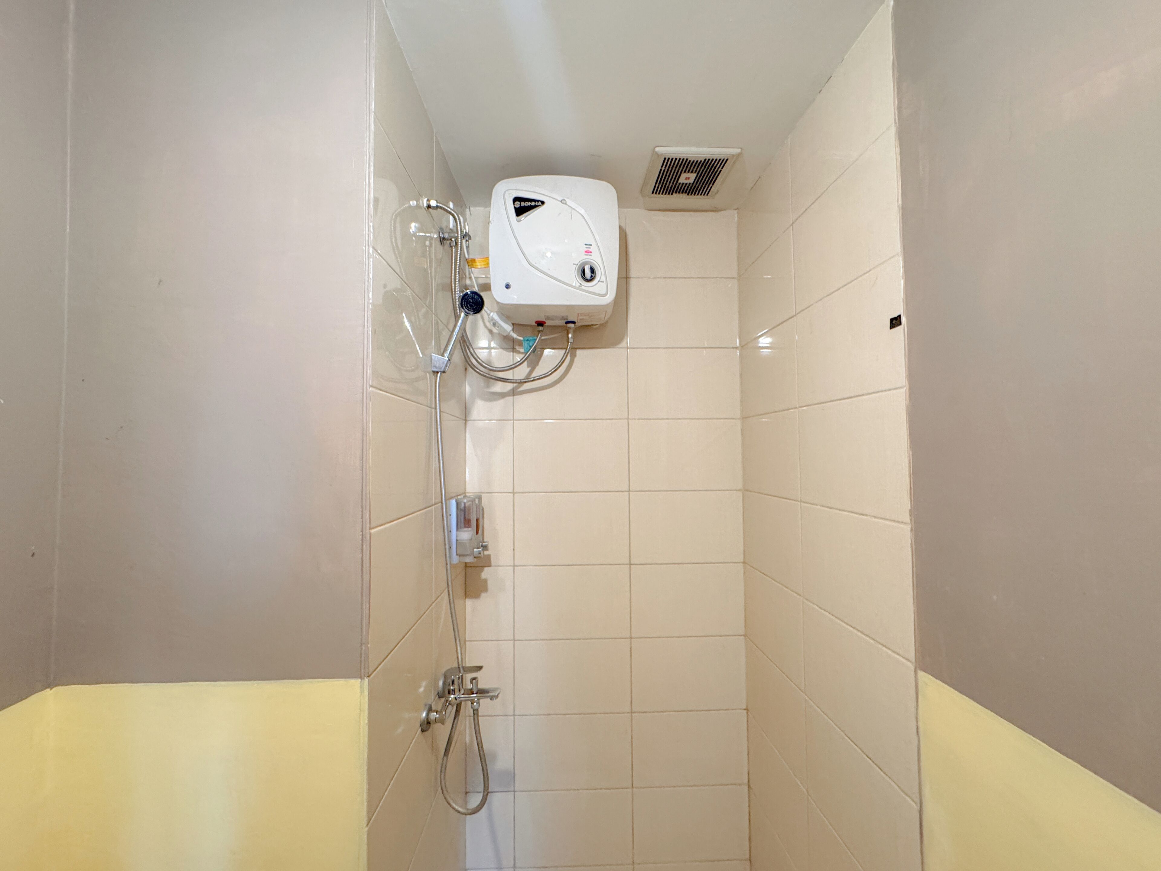 A small, tiled shower area with a handheld showerhead and a wall-mounted control panel.