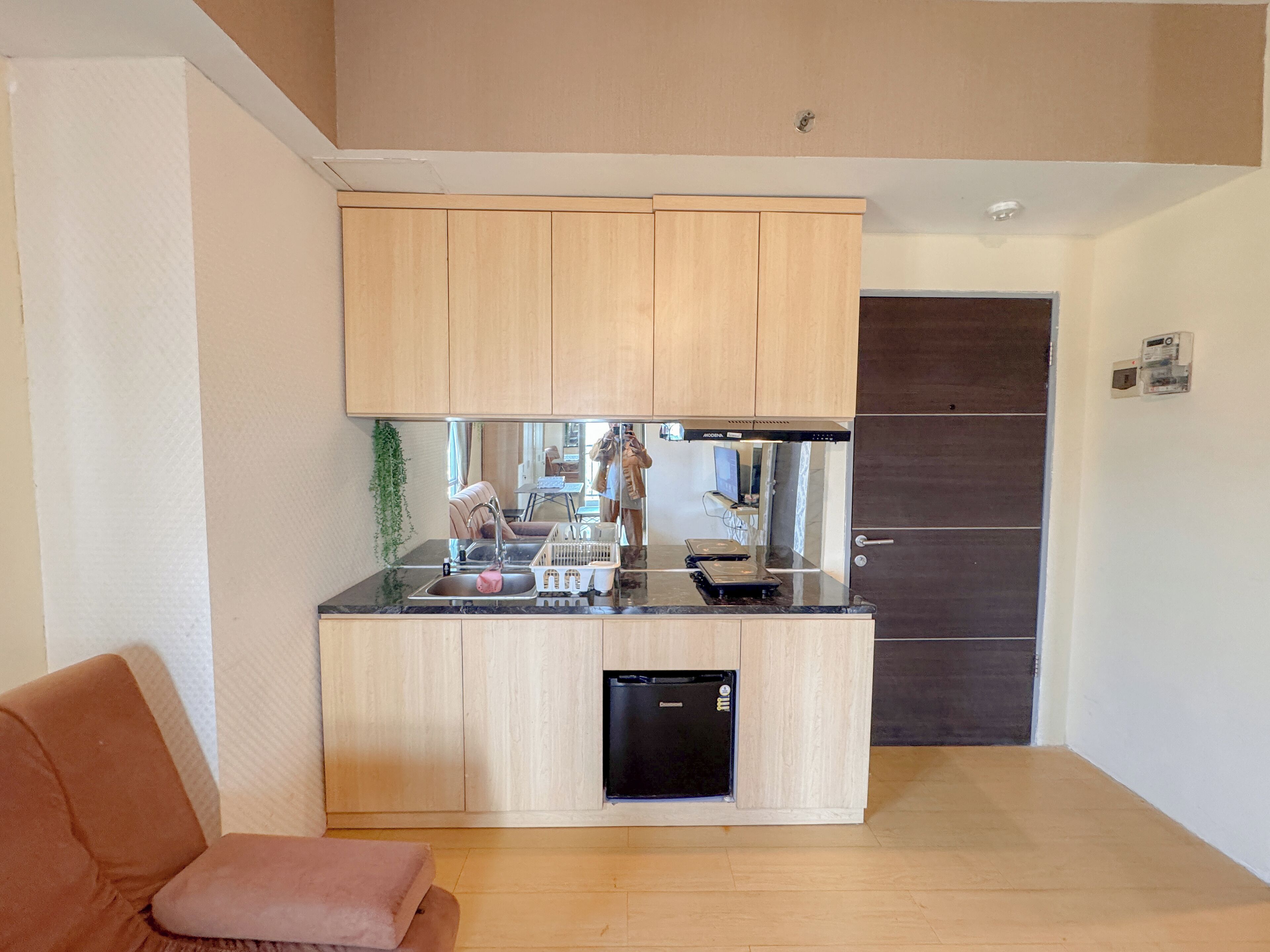 A compact kitchen with a built-in dishwasher, a sink, and a countertop with a kettle and a small appliance.