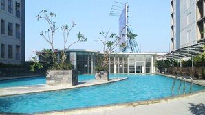 A swimming pool with a glass building in the background. - Simply And Good Place 2Br At Tamansari Prospero Apartment (Sidoarjo)