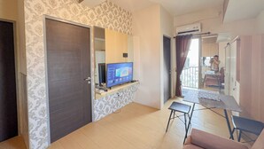 A living room with a TV, a sofa, a small table, and a door leading to a balcony. - Simply And Good Place 2Br At Tamansari Prospero Apartment (Sidoarjo)