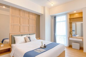 Ein Hotelzimmer mit einem großen Bett, einem hölzernen Kopfteil, einem Nachttisch, einem Spiegel, einem Fenster mit Vorhängen und einem kleinen Hocker.