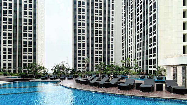 A swimming pool with lounge chairs and tall buildings in the background. - Comfortable 1Br Apartment At Pollux Chadstone (Cikarang)