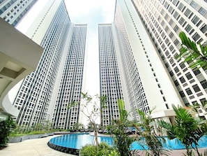 A high-rise building with a pool and lounge area. - Comfortable 1Br Apartment At Pollux Chadstone (Cikarang)