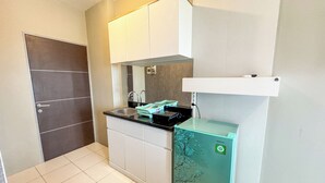 A compact kitchen with white cabinets, a black countertop, a built-in sink, and a green refrigerator. - Good Place And Tidy Studio At Tamansari Prospero Apartment (Sidoarjo)