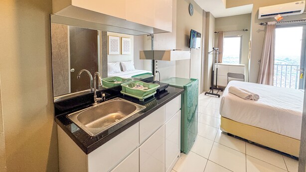 A hotel room with a kitchenette, a bed, a TV, and a balcony with a view. - Good Place And Tidy Studio At Tamansari Prospero Apartment (Sidoarjo)