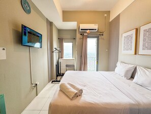 Una camera d'albergo con un letto, una televisione, un condizionatore d'aria e una finestra con tende.
