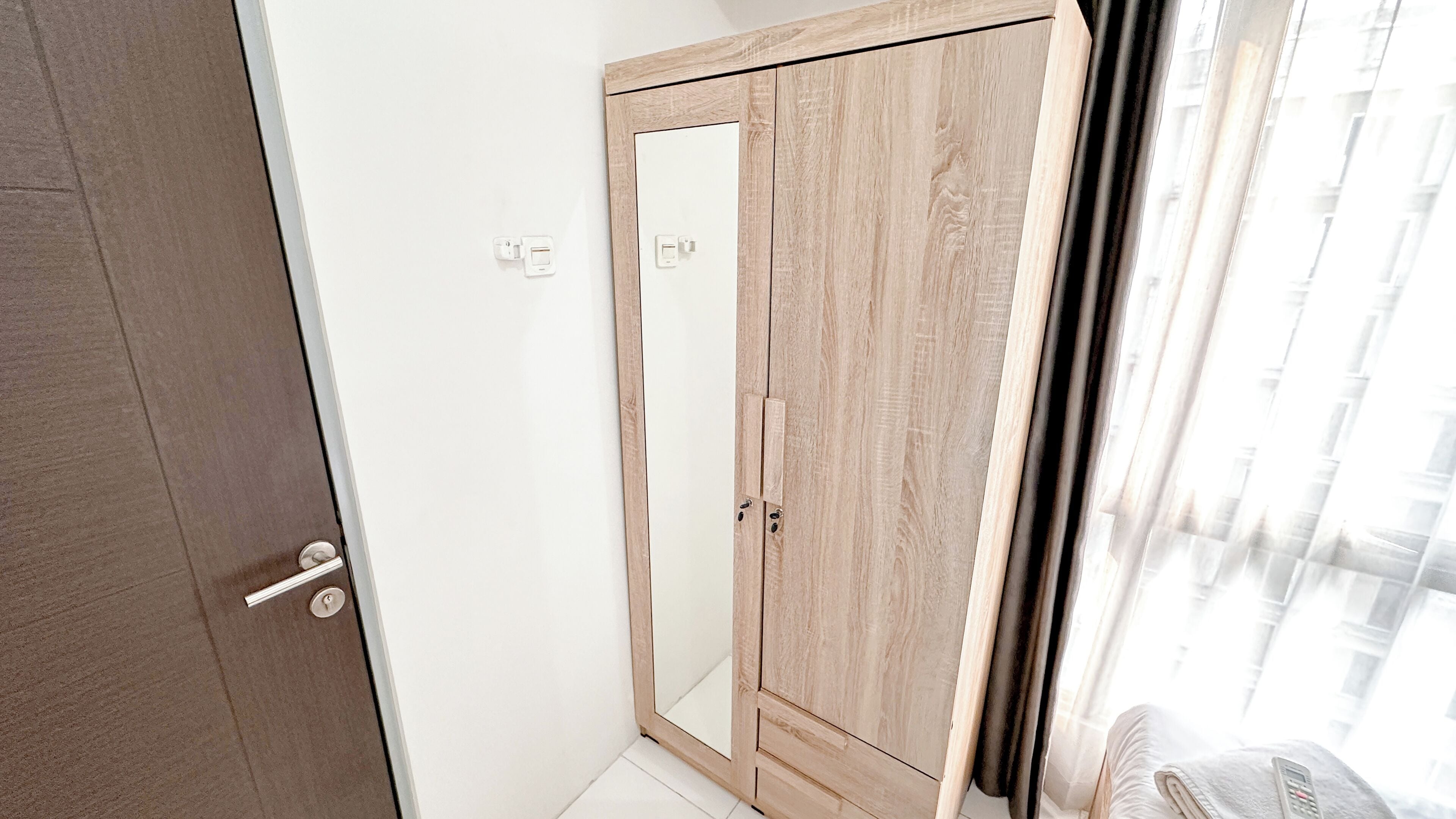 A room with a wooden wardrobe, a door, and a window with curtains.