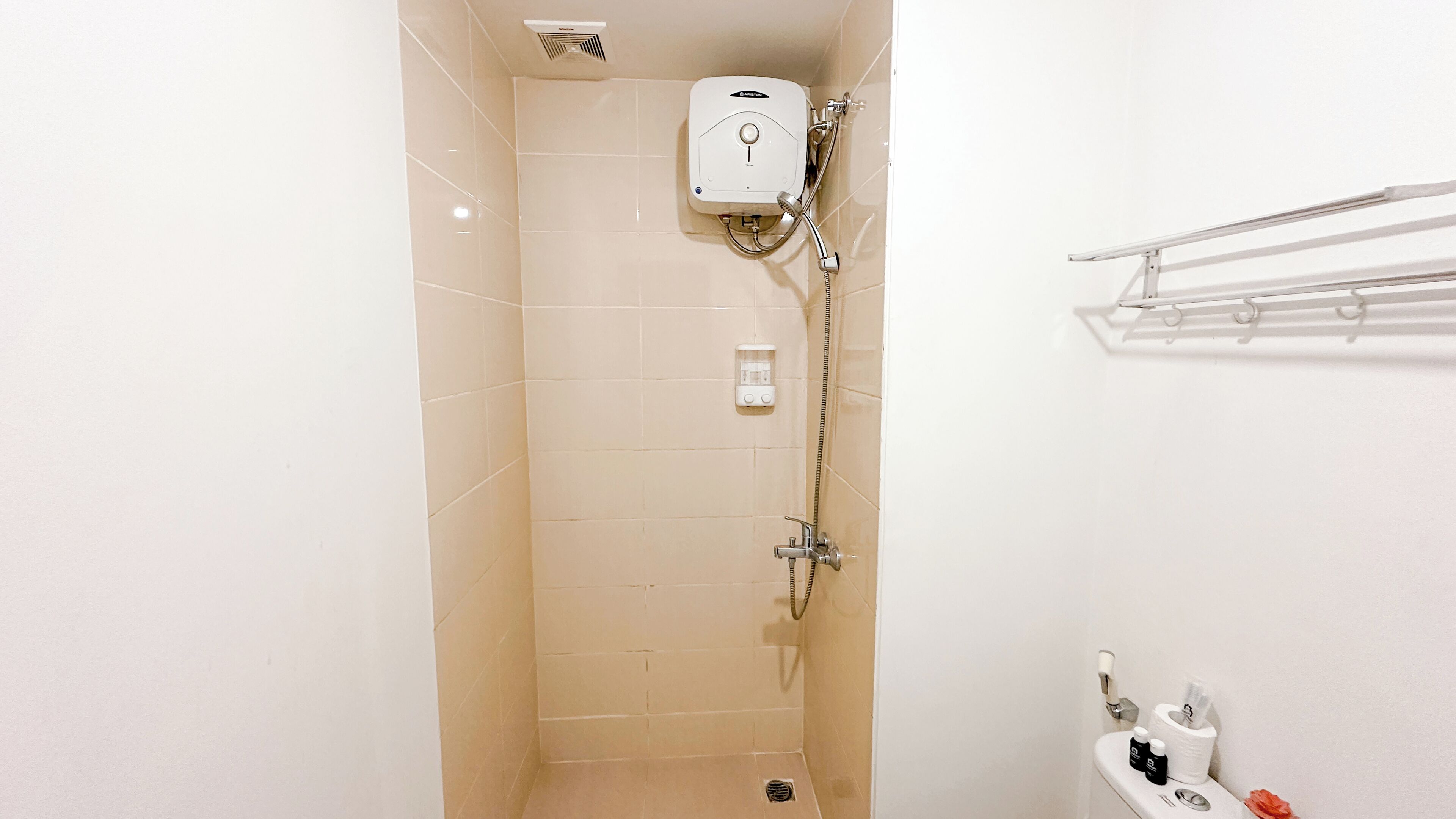 A small, tiled shower area with a handheld showerhead, a wall-mounted soap dispenser, and a towel rack.