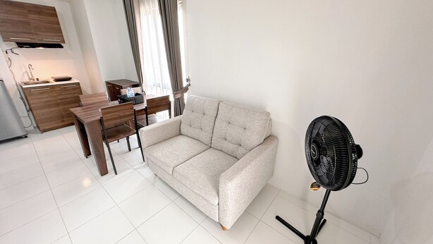 A modern living room with a sofa, a dining table, and a black standing fan. - Nice And Comfortable Stay 2Br At Tamansari Prospero Sidoarjo Apartment (Sidoarjo)
