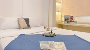 A hotel room with a bed, a blue throw blanket, a decorative tray with candles, and a Scandinavian-themed book on a nightstand. - Cozy And Modern 2Br At Meikarta Apartment (Cikarang)