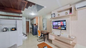 A modern living room with a flat-screen TV, a wooden coffee table, and a kitchen in the background. - Elegant And Spacious 2Br Loft Green Park Yogyakarta Apartment (Depok)