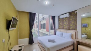 A hotel room with a large bed, a bedside table, a TV mounted on the wall, and a window with curtains. - Elegant And Spacious 2Br Loft Green Park Yogyakarta Apartment (Depok)