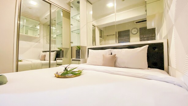 A modern hotel room with a large bed, a glass partition wall, and a view of the cityscape. - Good And Homey 1Br Apartment Mt Haryono Residence (Jakarta)