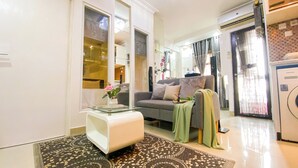 A modern living room with a glass coffee table, a grey sofa with a green throw, and a patterned rug. - Good And Homey 1Br Apartment Mt Haryono Residence (Jakarta)
