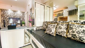 A modern living room with a sofa, a TV, and a kitchen area in the background. - Good And Homey 1Br Apartment Mt Haryono Residence (Jakarta)