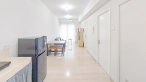 A hallway with a kitchen area on the left, a dining table with chairs, and a door on the right. - Homey And Compact 2Br Podomoro City Deli Medan Apartment (Medan)