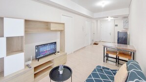 A modern living room with a flat-screen TV, a dining table, and a sofa. - Homey And Compact 2Br Podomoro City Deli Medan Apartment (Medan)