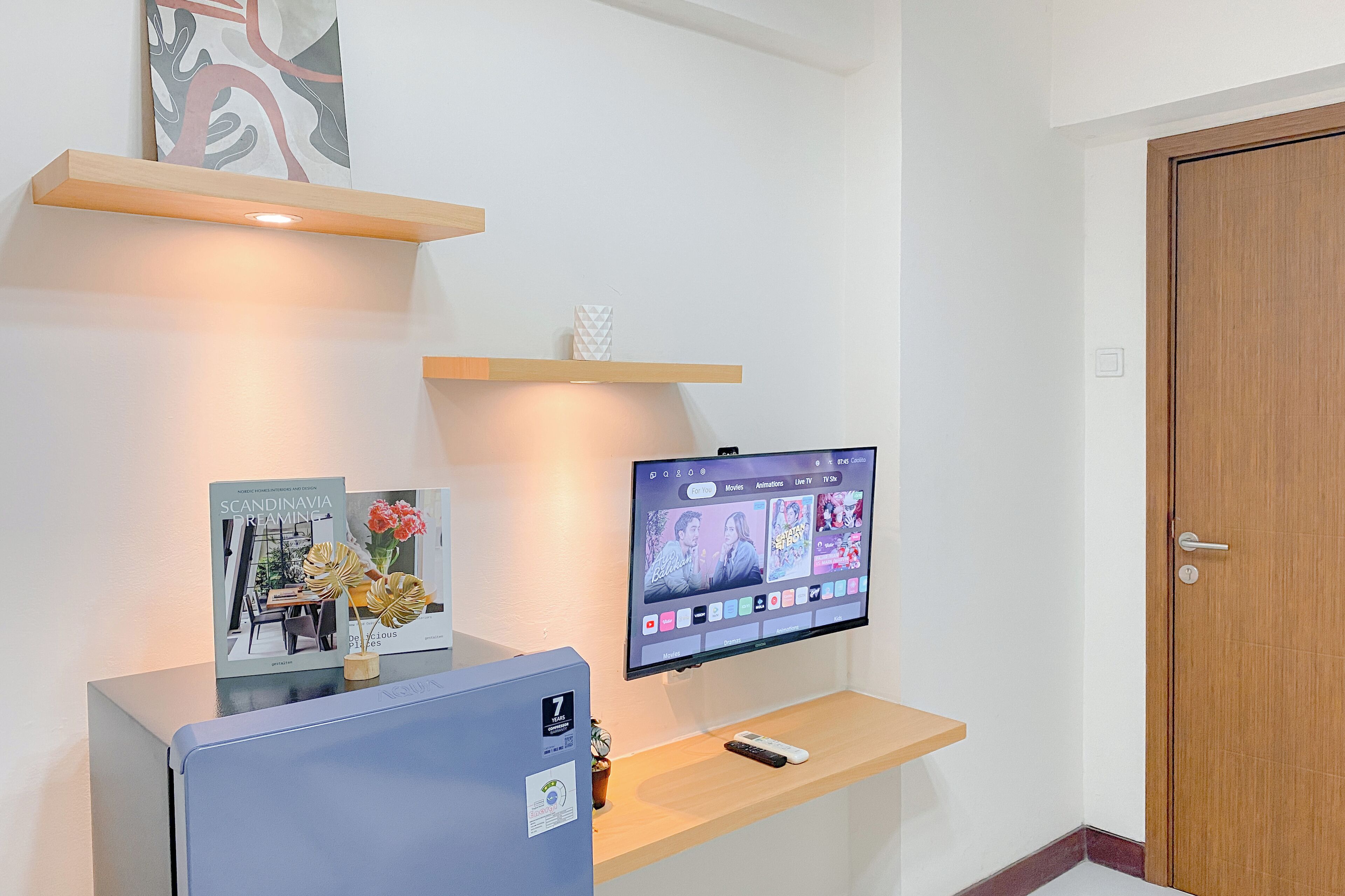 A reception desk with a computer, a television displaying movie options, and a door to the right.