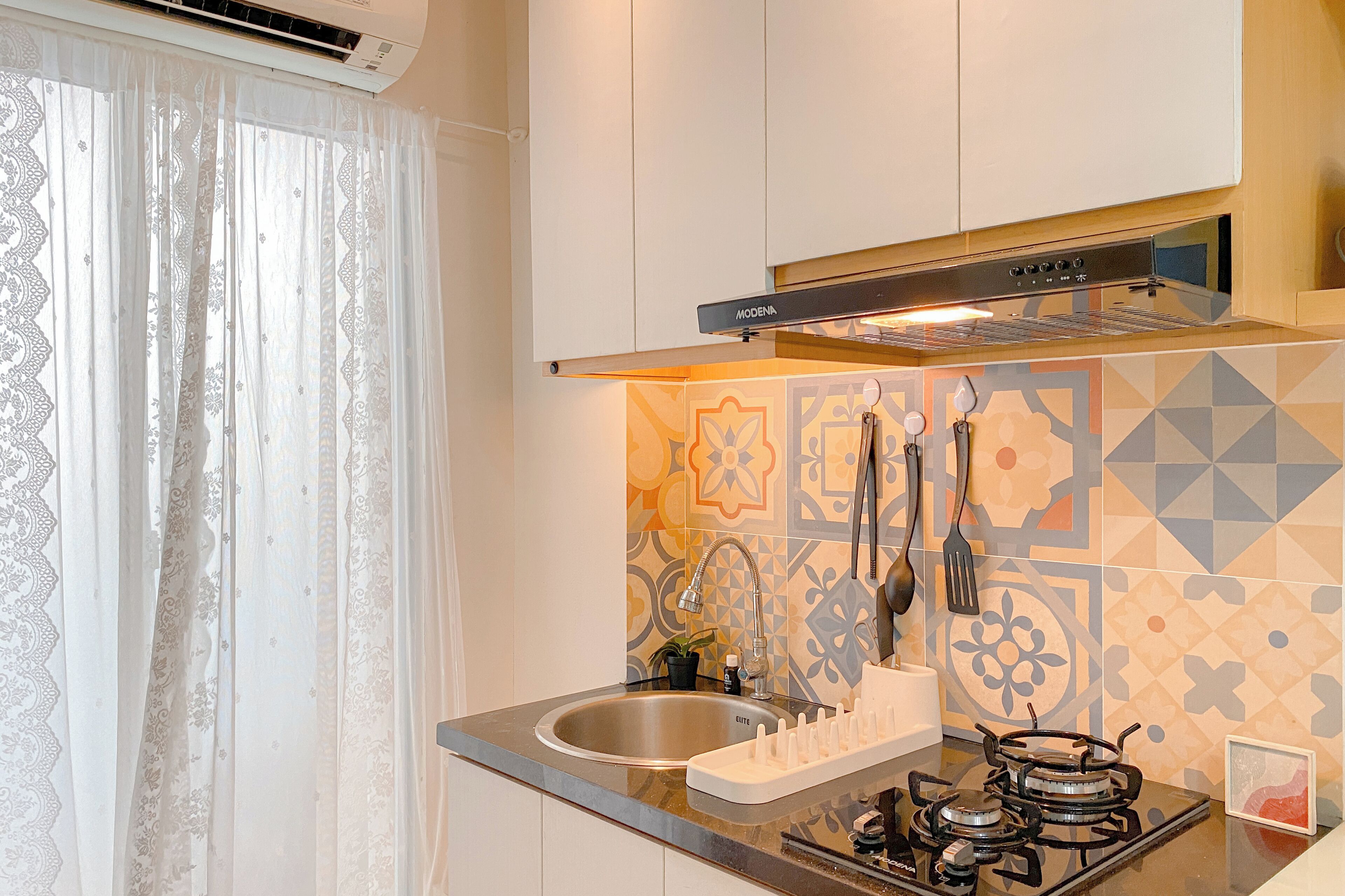 Una cocina con un lavaplatos de acero inoxidable, una estufa a gas, una campana extractora y un salpicadero decorativo.