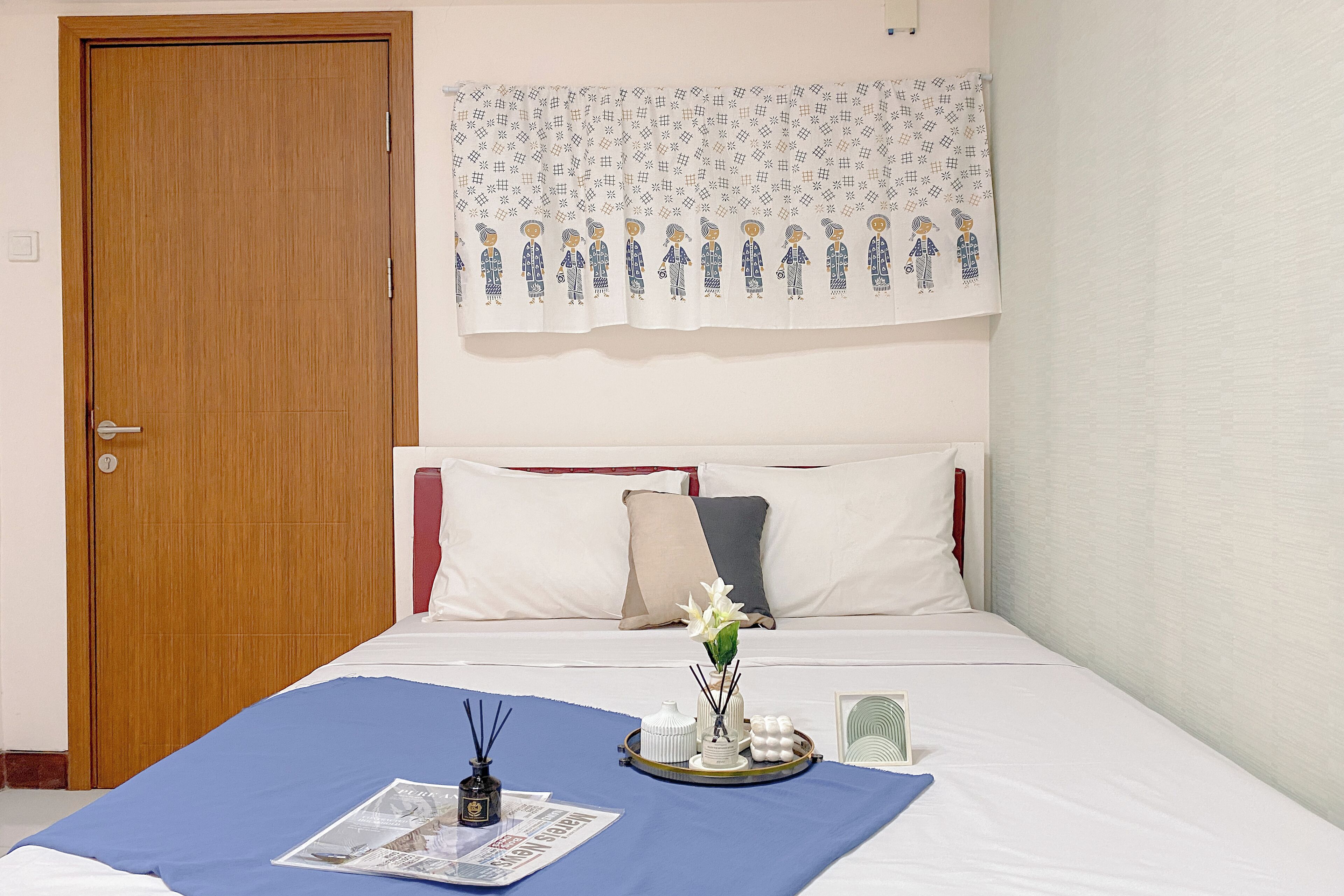 Ein ordentlich bezogenes Bett mit einer blauen Bettdecke, weißen Kissen und einer dekorativen Vase mit Blumen.
