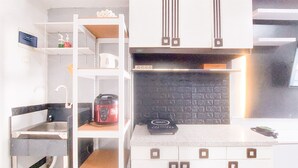 A compact kitchen with white cabinetry, a black backsplash, and a coffee maker on the counter. - Brand New Studio Apartment At Urbantown Serpong (South Tangerang)