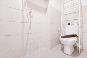 A bathroom with white tiles, a white toilet, and a shower area. - Brand New Studio Apartment At Urbantown Serpong (South Tangerang)