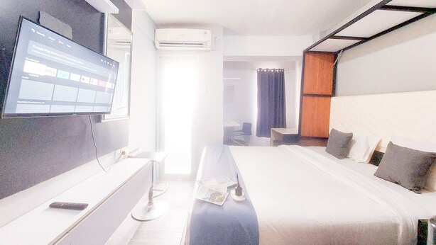 A hotel room with a bed, a desk, a flat-screen TV, and an air conditioning unit. - Brand New Studio Apartment At Urbantown Serpong (South Tangerang)