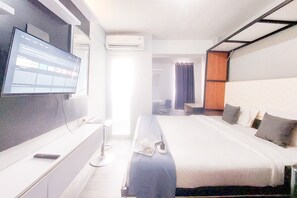 A hotel room with a bed, a desk, a flat-screen TV, and an air conditioning unit. - Brand New Studio Apartment At Urbantown Serpong (South Tangerang)