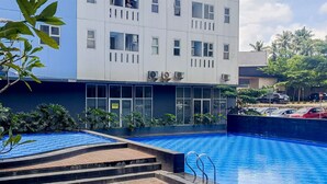 A modern building with a swimming pool, surrounded by greenery and a parking area. - Brand New Studio Apartment At Urbantown Serpong (South Tangerang)