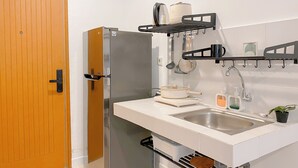 Eine kleine Küche mit einem Edelstahl-Kühlschrank, einer Spüle und einer Arbeitsplatte, auf der ein Wasserkocher und ein Topf stehen.