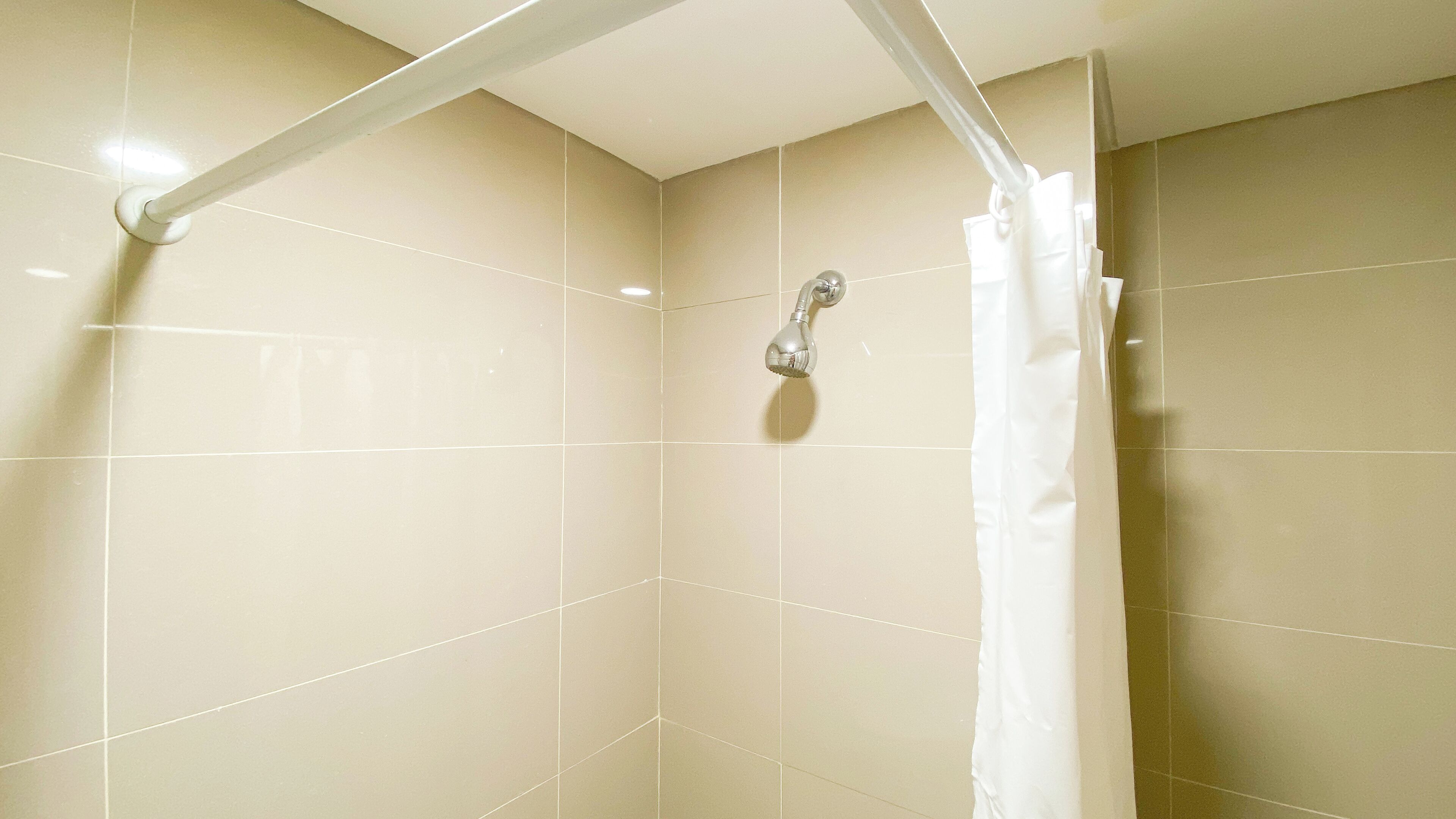 A shower with a white curtain, a handheld showerhead, and beige tiled walls.