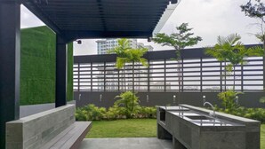 A modern outdoor patio with a concrete sink, a small garden area, and a view of a cityscape through a metal fence.