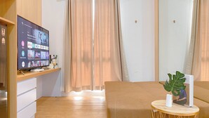 Ein modernes Wohnzimmer mit einem Flachbildfernseher, der eine Streaming-Dienstanwendung anzeigt, einer Couch, einem runden Holztisch mit einer Pflanze und einer kleinen weißen Kommode.
