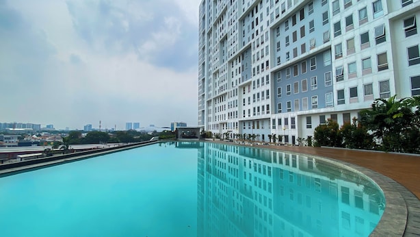 Ein großer, gewölbter Swimmingpool mit klar blauem Wasser, umgeben von einer Holzterrasse und einem hohen Wohnhaus mit vielen Fenstern.
