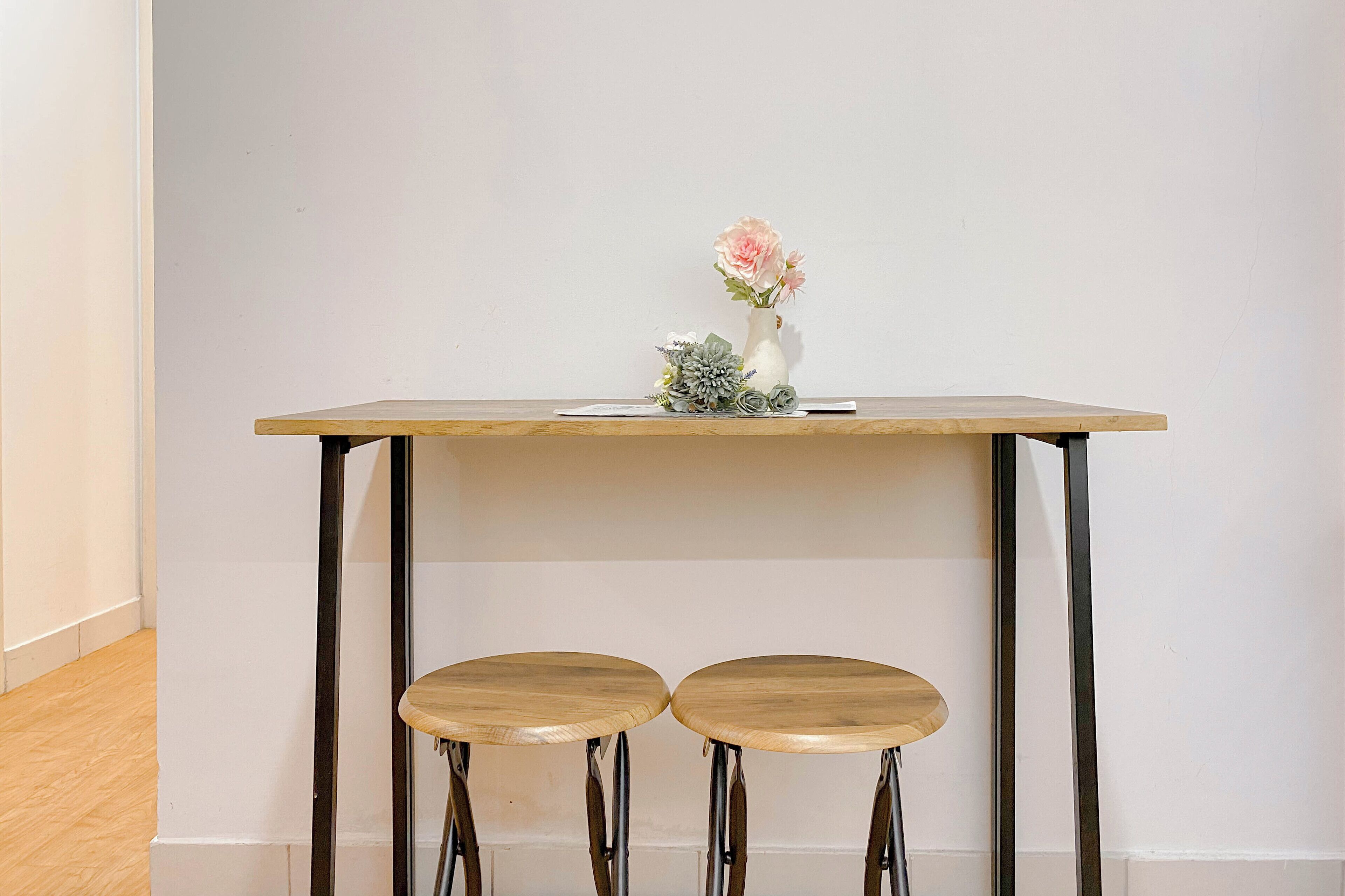 A small wooden table with two stools, a vase with flowers, and a book on the table.