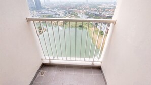 A balcony with a metal railing overlooking a cityscape, a body of water, and a green area.