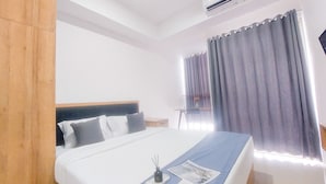 A hotel room with a bed, a nightstand, a desk, and a window with curtains.