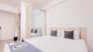 A hotel room with a large bed, a bedside table, a mirror, and a door. - Best Deal Studio Apartment Urbantown Serpong (South Tangerang)