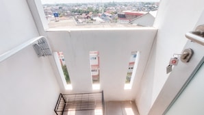 A narrow stairway with a metal handrail, a door with a lock, and a view of a residential area with houses and a water tower. - Best Deal Studio Apartment Urbantown Serpong (South Tangerang)