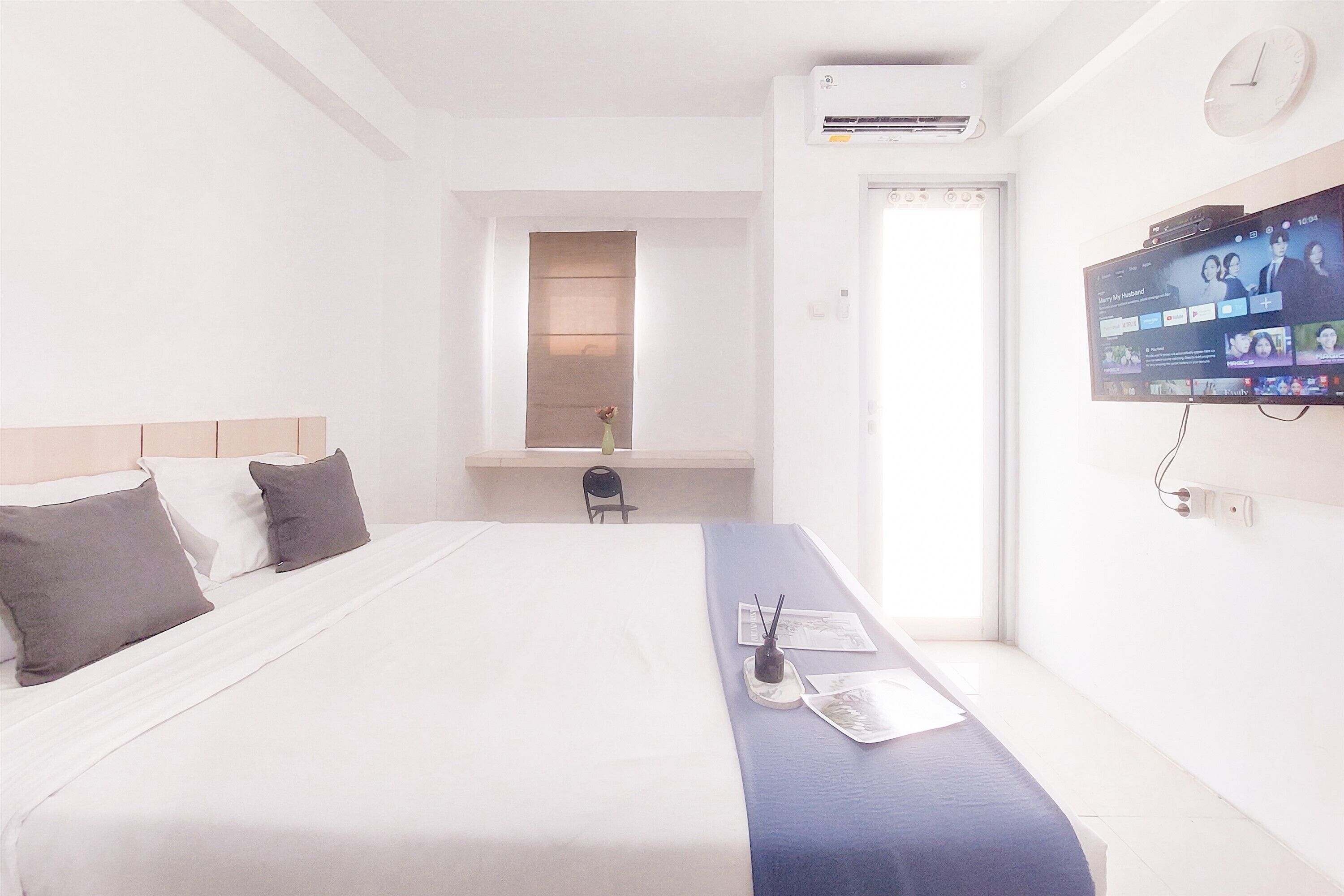 A hotel room with a large bed, a TV mounted on the wall, and a window with a view of the outside.