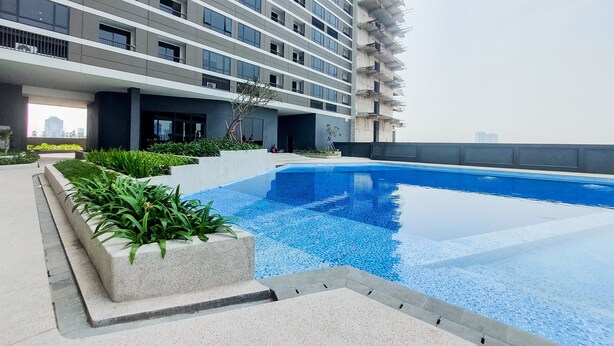A modern building with a rooftop swimming pool, surrounded by greenery and a cityscape view. - Comfort And Cozy Stay Studio Collins Boulevard Apartment (Tangerang)