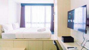 A hotel room with a bed, a TV, a desk, and a window with curtains. - Comfort And Cozy Stay Studio Collins Boulevard Apartment (Tangerang)