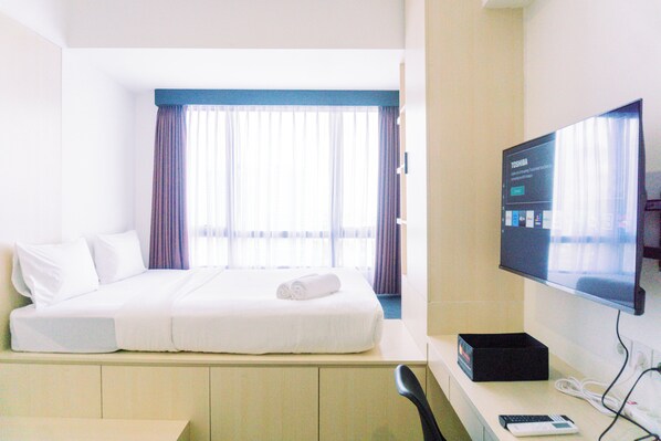 A hotel room with a bed, a TV, a desk, and a window with curtains. - Comfort And Cozy Stay Studio Collins Boulevard Apartment (Tangerang)