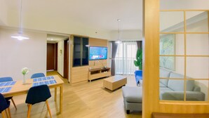 Una sala de estar moderna con una televisión de pantalla plana, una mesa de comedor con sillas, un sofá y un ventanal con cortinas.