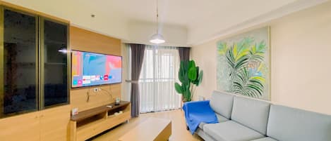 Ein modernes Wohnzimmer mit Flachbildfernseher, Couchtisch aus Holz, grauem Sofa und einer großen Pflanze.