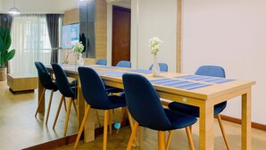 Un salón de conferencias con una larga mesa de madera, sillas tapizadas en azul y un jarrón blanco con flores.