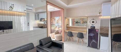 Una sala moderna con un sofá negro, televisor y área de cocina con microondas y pileta.