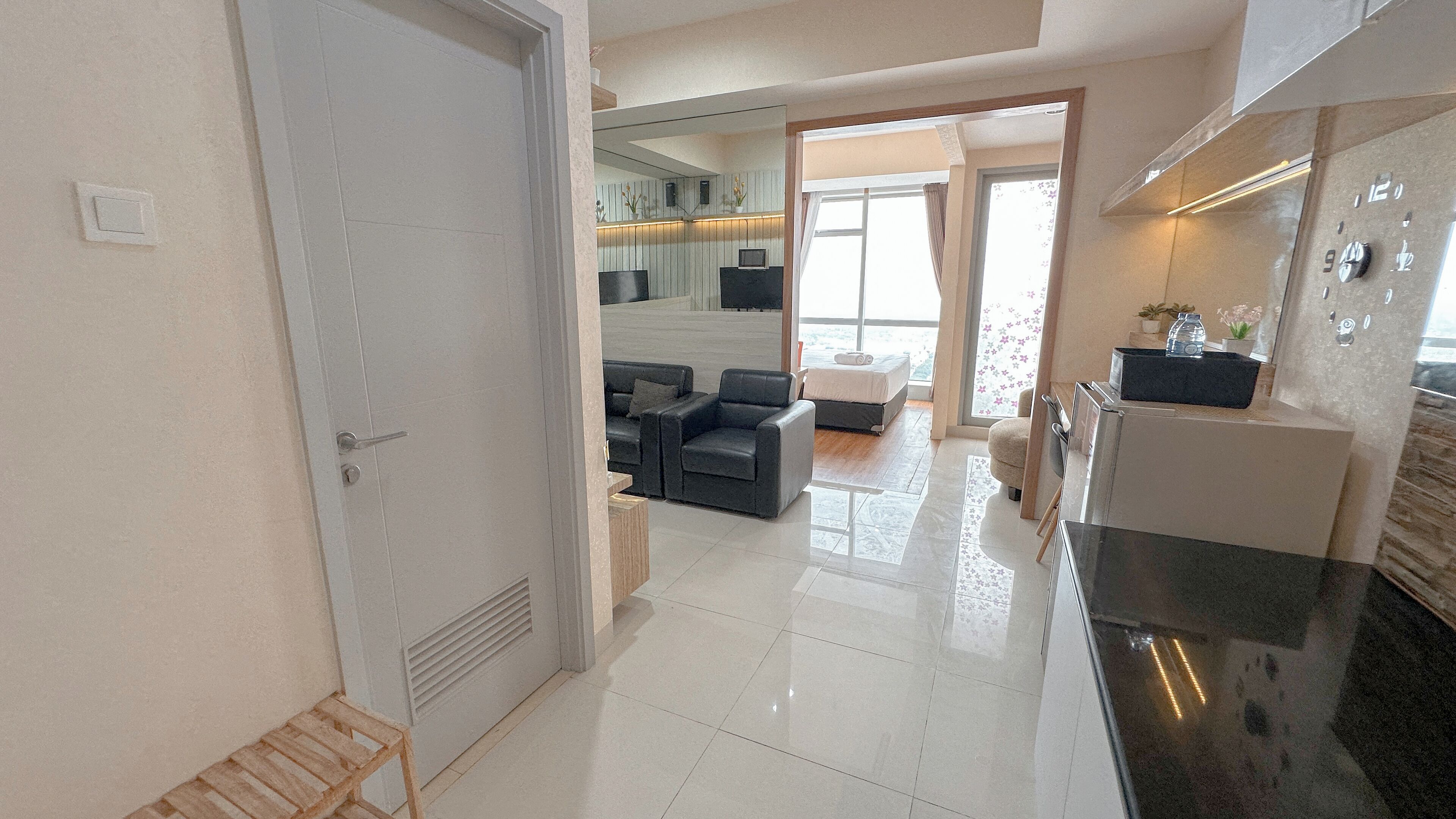 A modern kitchen with a refrigerator, stove, and sink. There is a dining area with a table and chairs. A living room with a sofa and a TV is visible through an open door.
